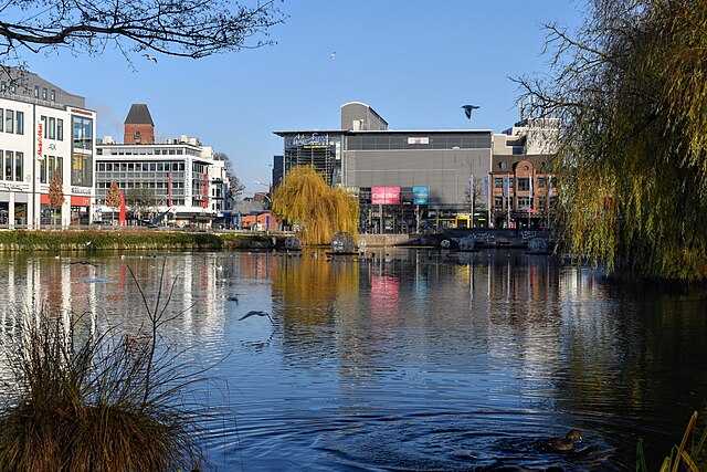 A view of the Neumünster pond in the city center, with the movie theater building ahead and the "Holsten-Gallery" mall on the left