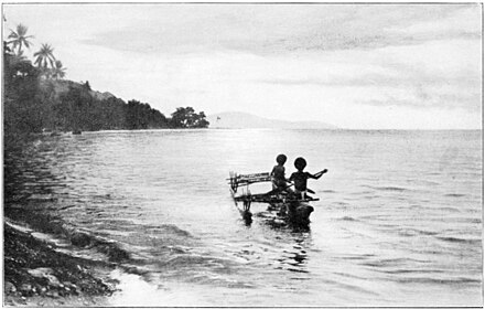 Two people in an outrigger canoes near a beach.