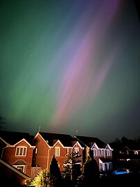 A purple and green aurora. Semi-detached houses can be seen