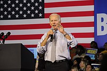 Photo of Biden holding a microphone at a campaign rally, with his jacket off and sleeves rolled up