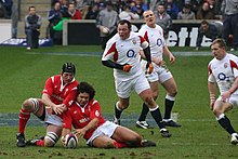 Two Wales' players falling onto a grounded ball while three England players approach their position.