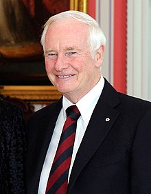 Photographie de Johnston souriant.  Il porte un costume sombre avec une cravate à rayures rouges et noires.