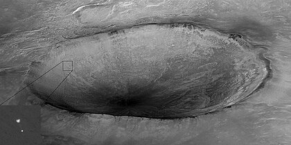 A câmera HiRISE da sonda espacial Mars Reconnaissance Orbiter (MRO) capturou esta imagem da Phoenix (canto inferior esquerdo) pendurada em seu paraquedas enquanto descia para a superfície de Marte. Aqui é mostrada uma cratera de 10 quilômetros de diâmetro informalmente chamada de "Heimdall", e uma imagem de resolução total aprimorada do paraquedas e do módulo de pouso. Embora pareça que a Phoenix está descendo na cratera, ela está, na verdade, cerca de 20 quilômetros na frente da cratera. Dada a posição e o ângulo de apontamento da MRO, a Phoenix está a cerca de 13 km acima da superfície, apenas alguns segundos após a abertura do paraquedas. Esta imagem mostra alguns detalhes do paraquedas, incluindo a lacuna entre as seções superior e inferior. No momento desta observação, a MRO tinha uma altitude orbital de 310 km, viajando a uma velocidade de solo de 3,4 quilômetros/segundo, e uma distância de 760 km para a sonda Phoenix. (definição 1 500 × 746)