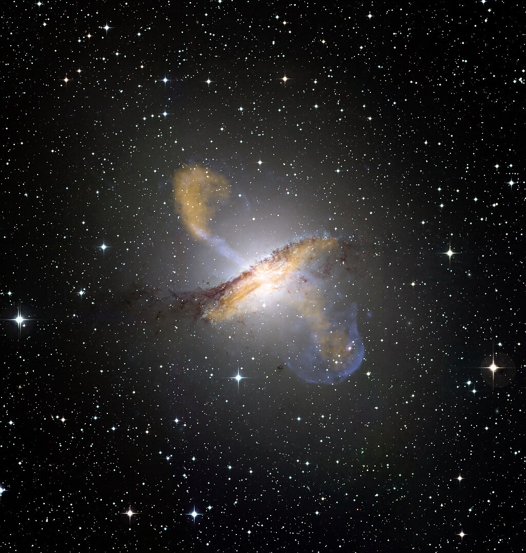 An astronomical image of Centaurus A, a galaxy with jets of plasma extending from its disk, generated by an active galactic nucleus located in the center of the galaxy. The image displays a mix of orange and blue hues, with a bright, elongated central disk surrounded by a faint, symmetrical structure extending outward. The image conveys the powerful energy and activity generated by the active galactic nucleus, and the dynamic nature of the universe.