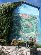 Photo de la fresque murale d'Irigny réunissant 3 éléments : La peinture, les végétaux et la lumière. Elle représente la commune avec différents personnages et monuments notables (L'abbé Pierre, Daisy Georges-Martin... Église, châteaux, tour de traille...)