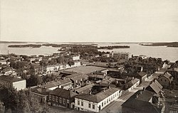 Kuva Kuopion tuomiokirkon tornista Väinölänniemen suuntaan. Kaupunginosan pohjoisraja kulkee kuvan etuosan taloissa (nykyinen Minna Canthin katu), Minna Canthin kotitalo Kanttila etualalla. Kuva on otettu vuosien 1889 ja 1893 välillä.