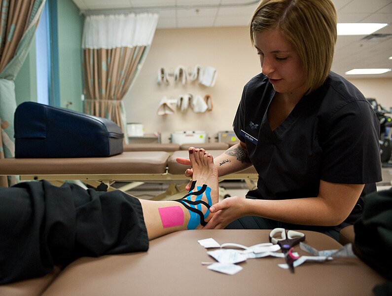A femal physical therapy technician, applies kinesio tape on a patient’s ankle to reduce swelling.