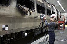 An NTSB investigator examines the damaged train car Kristin Poland sets up 3D Laser Scanner (16270957818).jpg