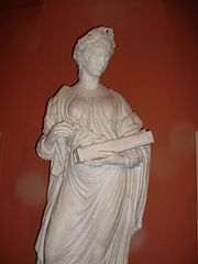 Statua greca a figura intera di una donna coronata di allori, tunica drappeggiata, strumento in mano (circa 50 cm).