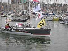 Un voilier noir et blanc avance au moteur dans un port. Sur la coque, on peut lire « Faber France » et « Dunkerque communauté urbaine ».