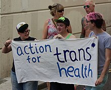 Trois personnes tenant une banderole sur laquelle est écrite {{lang|en|Action for trans health}}.