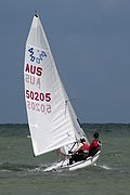 A 420 sailing dinghy as it crests a wave, one sailor out on the trapeze.