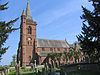 Une église en grès avec, à gauche une tour avec une flèche et une tourelle d'escalier, et à droite le corps de l'église avec un clerc