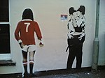 Två poliser som kysser varandra, medan fotbollsspelaren, George Best (Manchester United) tittar på, Brighton