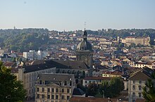 Veduta del campanile della chiesa in mezzo ai tetti della città.  Edifici sul versante della valle in fondo.