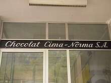 На этом рисунке показана надпись Chocolat Cima-Norma SA курсивом (белая на темном фоне), которая прикреплена к стеклянной двери.