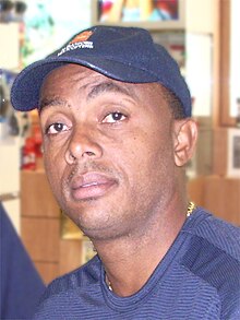 A young black man, in a baseball cap, looking ahead, in a black training top