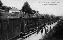 Înainte de 1914, un tren a fost oprit în gară, cu locuitori pe peron care pozează pentru fotograf.  Clădirea pasagerilor este vizibilă în partea de sus a șanțului.