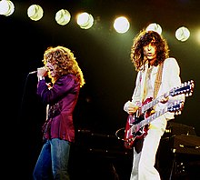 Een kleurenfoto van Robert Plant met microfoon en Jimmy Page met een dubbelhals gitaar op het podium.