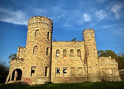 The front of a yellow limestone castle with castellated towers is covered in spraypainted graffiti.