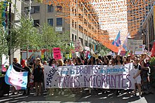 O mulțime de oameni în spatele unui banner pe care scrie „Martie pentru drepturile migranților trans”
