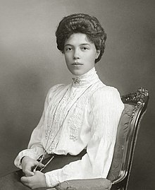 Black-and-white photograph of a young Olga seated in an Edwardian dress with a high neck line and long sleeves. Her thick dark hair is pinned up, and she wears a rope of pearls around her neck.