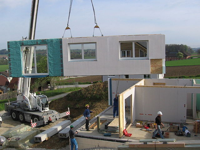 Wall of a prefab house being placed by a crane.