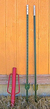Two T-posts and red post pounder (or driver) used to drive them into the ground. The flat plate helps stabilize the post, which is driven into the ground until the plate is buried.