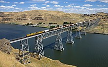 A freight train crosses a wide river on a steel bridge