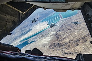 מבעד לפתח של מטוס תדלוק ניתן לראות מטוס F-35I אדיר ישראלי (מימין) של טייסת 140 ושני מטוסי F-35A אמריקאים, מטוסי הקרב עפים מעל בריכות המלח של ים המלח, והרי מדבר יהודה.