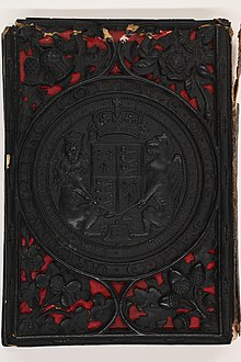 A book cover sculpted in black papier-mâché depicting a large crest of the British Empire surrounded by acorns, roses, thistles, and shamrocks.