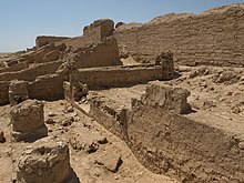 Foto colorida.  No deserto, restos de pedra lavrada estão em primeiro plano.