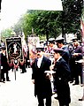 Photo en noir et blanc montrant des hommes en casquette, à l'arrière-plan deux hommes tiennent des bannières