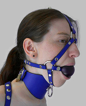 A model wearing a head harness with a ball gag and posture collar