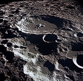 A grey, many-ridged surface from high above. The largest feature is a circular ringed structure with high walled sides and a lower central peak: the entire surface out to the horizon is filled with similar structures that are smaller and overlapping.