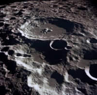 A grey, many-ridged surface from high above. The largest feature is a circular ringed structure with high walled sides and a lower central peak: the entire surface out to the horizon is filled with similar structures that are smaller and overlapping.