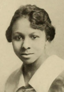 A young Black woman with short hair, wearing a wide white collar