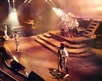Queen árið 1984. John Deacon (til vinstri), Freddie Mercury (á miðju sviði), Brian May (neðst á myndinni), Roger Taylor (trommur)