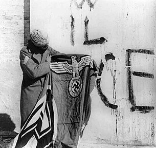 A Sikh soldier with the flag of Nazi Germany after German surrender during World War II. Sikh soldier with captured Swastika flag.jpg