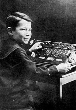 קורט הרצשטרק בן ה-8 מדגים, בתערוכת ציוד משרדי בווינה ב-1910, מכונת חישוב מכנית מהמפעל של אביו