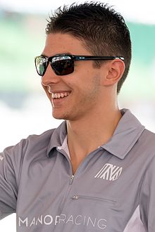 Photographie d'un homme brun, souriant, vu de trois-quarts, en gros plan, avec des lunettes de soleil.