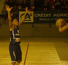 Edwige Lawson im Trikot der französischen Mannschaft mit erhobenen Armen in einer defensiven Position.