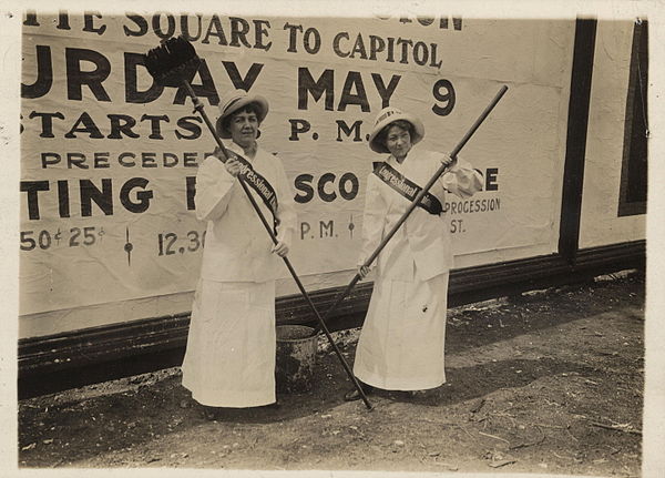 Members of the CUWS holding brushes in front of a large billboard, 1914