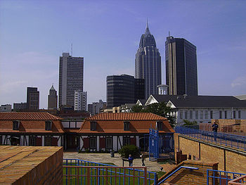 Linha do horizonte de uma cidade, mostrando muitos edifícios altos de alturas variadas ao fundo;  Um conjunto de prédios baixos e um pequeno parque são visíveis em primeiro plano.