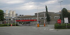 Un bâtiment industriel gris à trois étages, avec trois drapeaux "Nidar" à l'entrée.