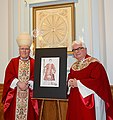 Bishop Richard J. Malone and Msgr. David S. Slubecky beneath a calendar reliquary (tapestry) of 365 saints and icon of Saint Caesarius of Terracina