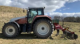 Zijaanzicht van tractor met daarachter diepwoeler in een weide