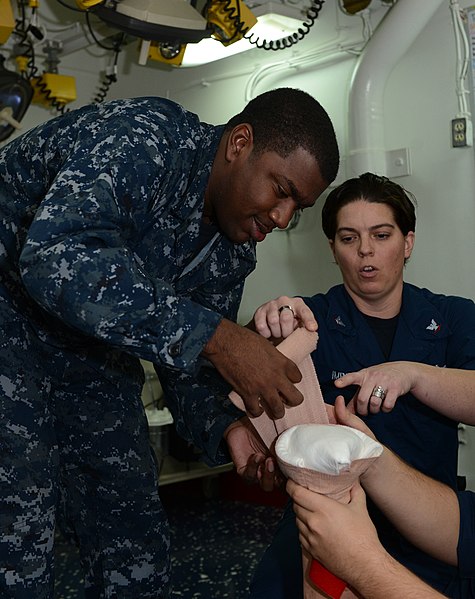 File:U.S. Navy Electronics Technician 3rd Class Jennifer Imbimbo shows Yeoman 3rd Class Jarvis Bamberg how to apply a bandage to a severed arm during a training exercise aboard the amphibious assault ship USS Bataan 131002-N-HQ940-012.jpg