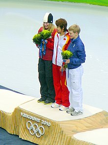 Les trois médaillées olympiques sur la première marche du podium, portant leurs bouquets de fleurs.
