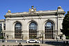 An ornate stone building with three tall arched entrances and a clock in the middle of the top